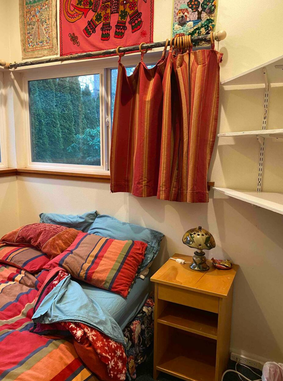 Room interior with colorful bedding, a window, and a shelf.